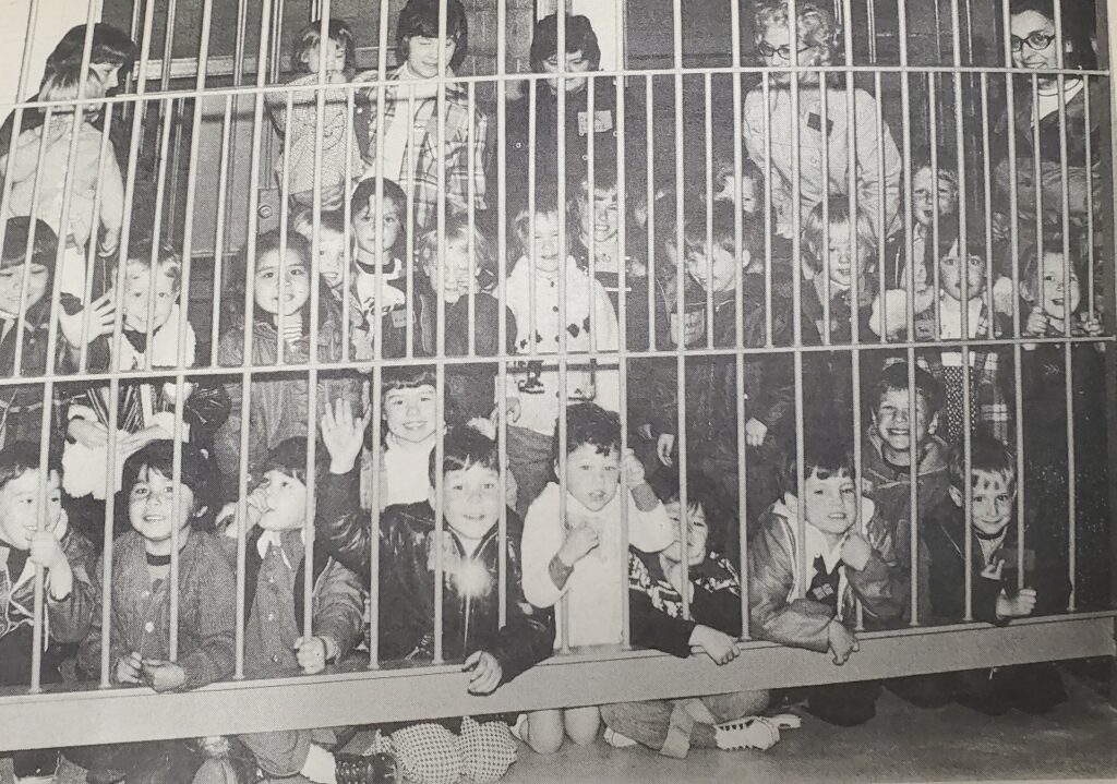 A group of school children on a field trip pose for a photo behind jail bars.